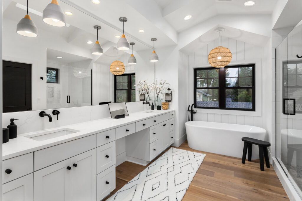 bathroom declutter Spacious modern bathroom with a large vanity featuring two sinks and white cabinetry. The room has a freestanding bathtub, a glass-enclosed shower, and a mixture of pendant and natural lighting. A black stool and a geometric rug add decorative touches.