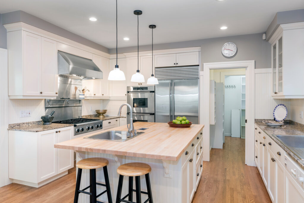 Declutter your home Bright, airy kitchen with a large wooden island and hanging pendant lights. The kitchen includes white cabinets, stainless steel appliances, and a double-door refrigerator. The hardwood flooring and walk-in pantry contribute to a welcoming atmosphere.